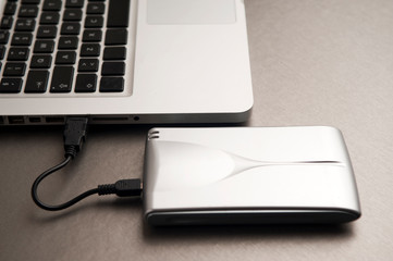 silver external hard drive, partial laptop view, on aluminum table