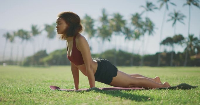 Young attractive african american woman doing morning yoga in a sunny park, female body wellness concept