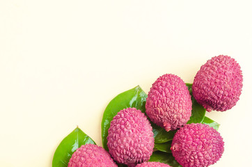 top view on unpeeled ripe exotic tropical lychee fruit in shell with green leaves on yellow background closeup, from Thailand, China for making dessert and wine, copy place for text