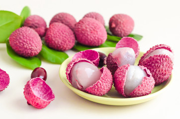peeled ripe exotic tropical lychee fruit close up, in shell, with seeds, pulp, green leaves soft focus, on yellow background, from Asia for making dessert and wine