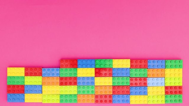 Colorful bricks making wall on pink background - Stop motion