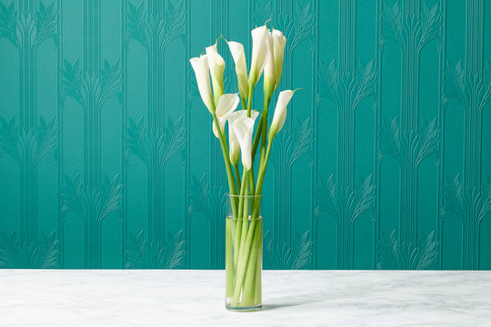 Calla Lilly Bouquet in Glass Vase on Marble Table Surface Against Art Deco Designer Wall Paper  