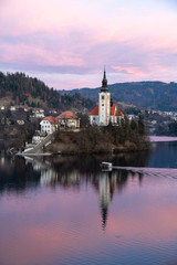 Fototapeta na wymiar Island Church at Lake Blend in Slovenia during Sunrise. A Pletna boat is transporting tourists.