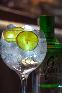 Gintonic con lim&oacute;n y botella de Ginebra al fondo