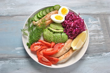 Chicken salad with avocado , tomatoes, red cabbage, cucumbers, boiled eggs and parsley. Healthy lunch bowl with vegetables and chicken on wooden background Healthy food concept