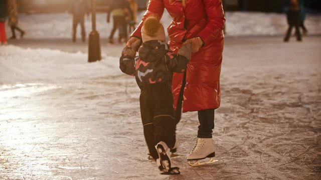 A young woman skating on the ice rink with her little child - playing outdoors