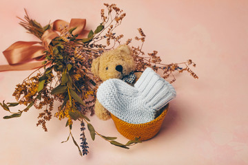 Knitted baby bootee, toy bear and flowers on soft pink background. Birth of a baby concept.