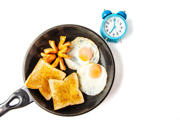 Breakfast. Fried eggs, sausages and fried toasts in a frying pan and a blue clock. The clock telling the time at 7:00 am.  Image on top view.