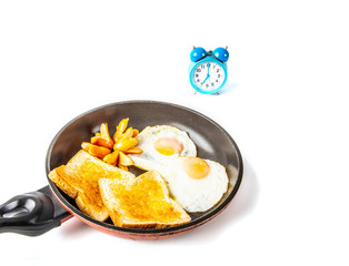 Breakfast. Fried eggs, sausages and fried toasts in a frying pan and a blue clock. The clock telling the time at 7:00 am