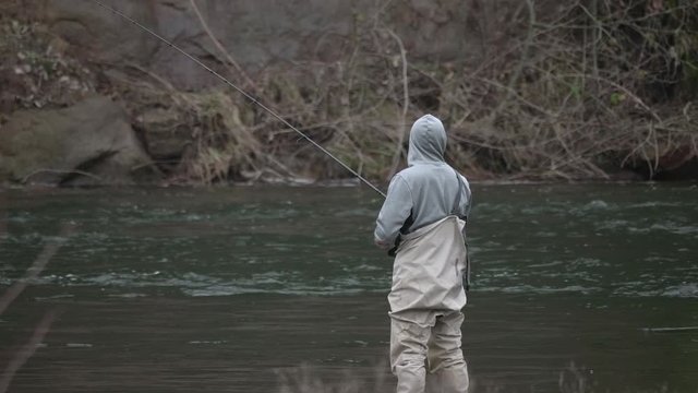 Male in waders alone fishing in peace reeling in lure on river water bank on sandy river in pacific northwest oregon in slow motion