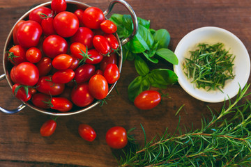 Overflowing bowl of vibrant cherry tomatoes and fresh herbs on rustic timber chopping block in an organic produce flat lay