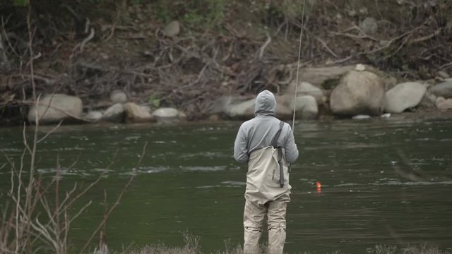 Male in waders alone fishing peacefully with lure on river water bank on sandy river in pacific northwest oregon in slow motion