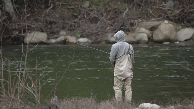 Male in waders alone fishing peacefully reeling in and casting lure on river water bank on sandy river in pacific northwest oregon in slow motion