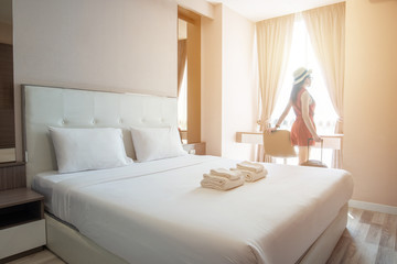 Tourist woman standing nearly window with her luggage in hotel bedroom. - obrazy, fototapety, plakaty