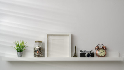 Cropped shot of mock up frame, camera and decorations on white shelf with white wall background