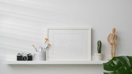 Close up view of mock up frame, camera and decorations on white shelf with white wall background