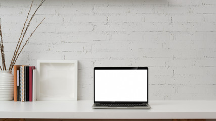 Close up view of blank screen laptop, mock up frame, books and decorations on white table with brick wall background