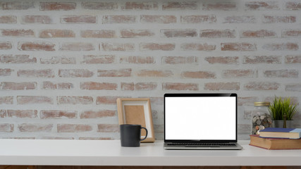 Cropped shot of blank screen laptop, mock up frame and decorations on white table with brick wall background