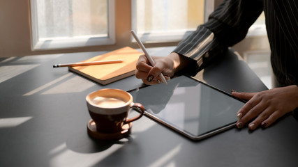 Cropped shot of female using mock up digital tablet in dark modern workplace