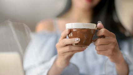 Close up view of a woman holding morning coffee in living room