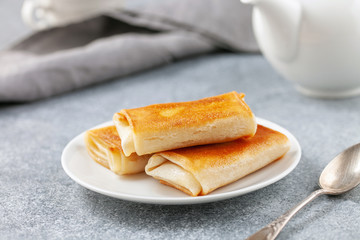 Pancakes envelopes with curd or ricotta in a plate on a grey background