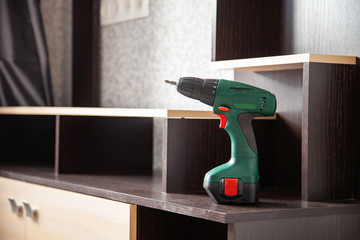 A screw or drill stands on the cabinet shelf. Concept of repair and assembly of furniture in the house