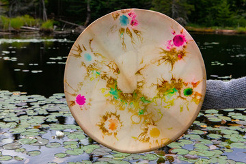 Closeup of young shamanic woman hand holding sacred native frame drum on lake with waterlilies in...