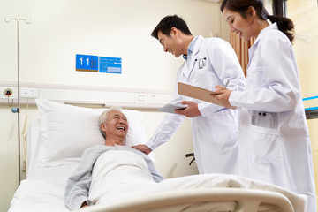 two young asian doctors talking old man at bedside