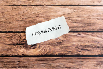 Commitment text on torn paper on top of wooden background.