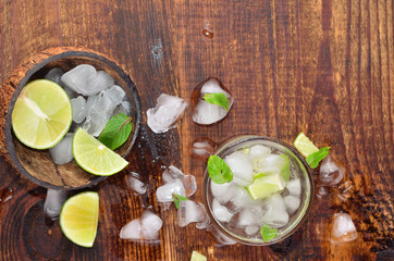 mojito with ice and additives in a coconut shell on a wood background top view