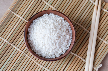 White rice grits in a clay Cup and wooden sticks on the table, top view