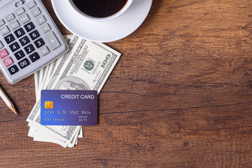 Top view of a blue credit card placed on money US dollars near pencil, calculator and coffee cup on...
