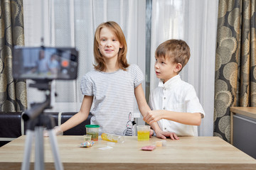 Naklejka premium Cute little bloggers with homemade slime recording vlog video on kitchen.