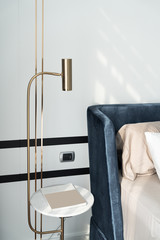 Bedroom corner navy blue velvet bed with soft pillows setting decorated with circular marble night table and navy blue paint wall in the background / cozy interior design