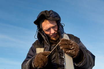 A worker in a blue jacket sharpens a chainsaw chain.