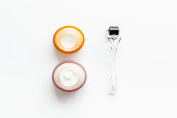 Dermaroller for mesotherapy near creams on white background top-down flat lay