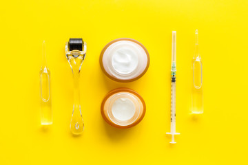 Dermatologist work desk with tools. Dermaroller, syringe, ampoule on yellow background top-down flat lay