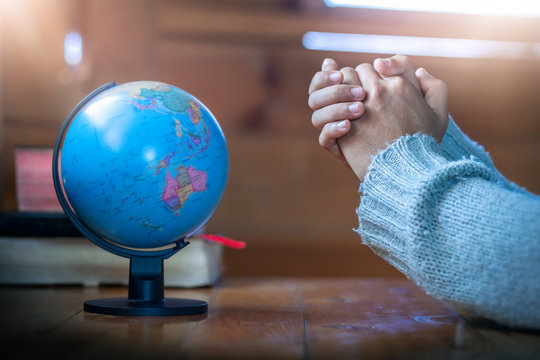 Close up hands praying for globe on wooden table, christian concept. - Powered by Adobe