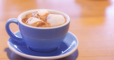 Drink Hot Chocolate topped by Milk Latte Foam with marshmallow in blue ceramic porcelain cup on wooden table background. Relaxed moment with healthy dairy beverage with melted sweets in morning.