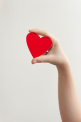 Fototapeta premium Child's hand holding red heart over white background