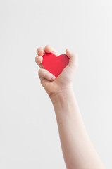 Child's hand holding red heart over white background