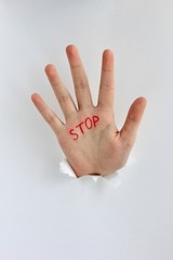Hand with text stop written on the palm showing stop gesture through a hole in paper. Gestures,...