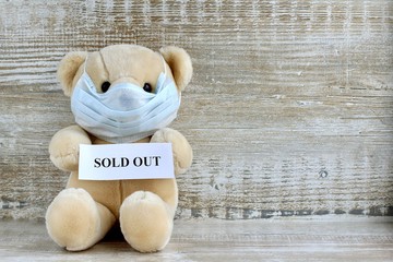 Announcement with text sold out held by a toy Teddy bear in a protective medical mask on a wooden...