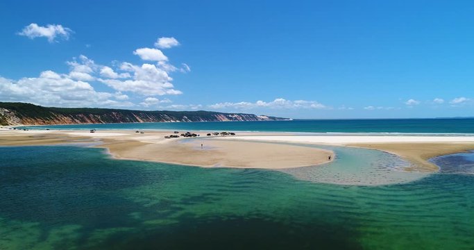 4k ascending hovering aerial view of recreational vehicles and holiday makers at Double Island Point with the coloured sand dunes near the town of Rainbow Beach at low tide,Queensland,Australia