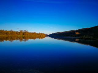autumn day, clear bright blue sky reflected in the river, one bank of the river is in shadow, the other is illuminated by the sun, autumn