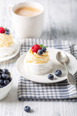 Delicious Pavlova cake with whipped cream and fresh berries. White cup of coffee. Selective focus