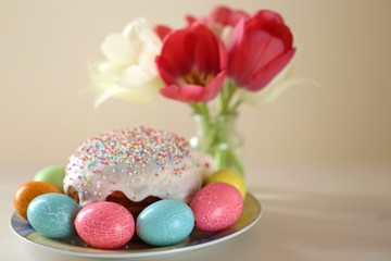 Easter holiday.Easter holiday. Multicolored eggs and Easter baking, tulip flowers in a vase on a  beige background.Spring festive religious background.