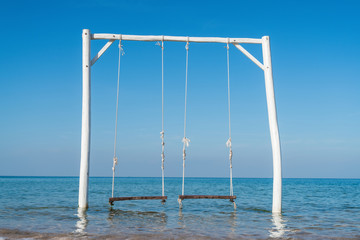 Fototapeta na wymiar Empty swing on tropical beach with blue sky