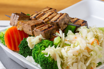 A closeup view of Japanese teriyaki tofu skewers over a bed of steamed vegetables.