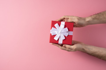 Valentine's Day celebration concept. A nice gift from a loved one. Box with a bow in male hands on a delicate pink background. Copy space. Flat lay.